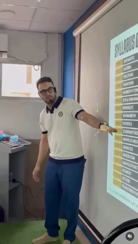 A teacher explaining the mathematics syllabus beside a projected screen