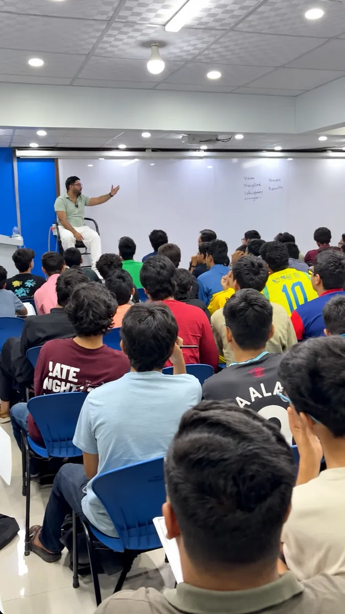 Students listening to a teacher in a classroom with a large whiteboard