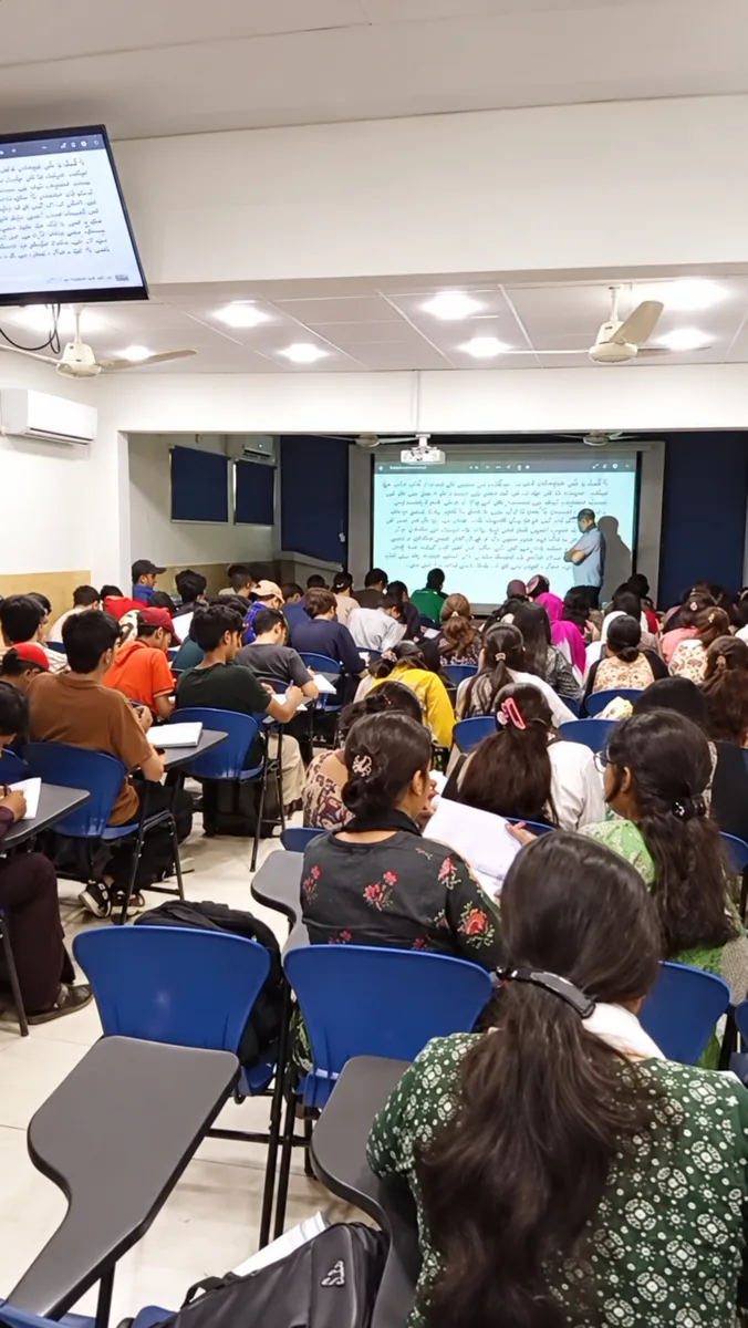 Students taking notes during a lesson with projected Urdu text