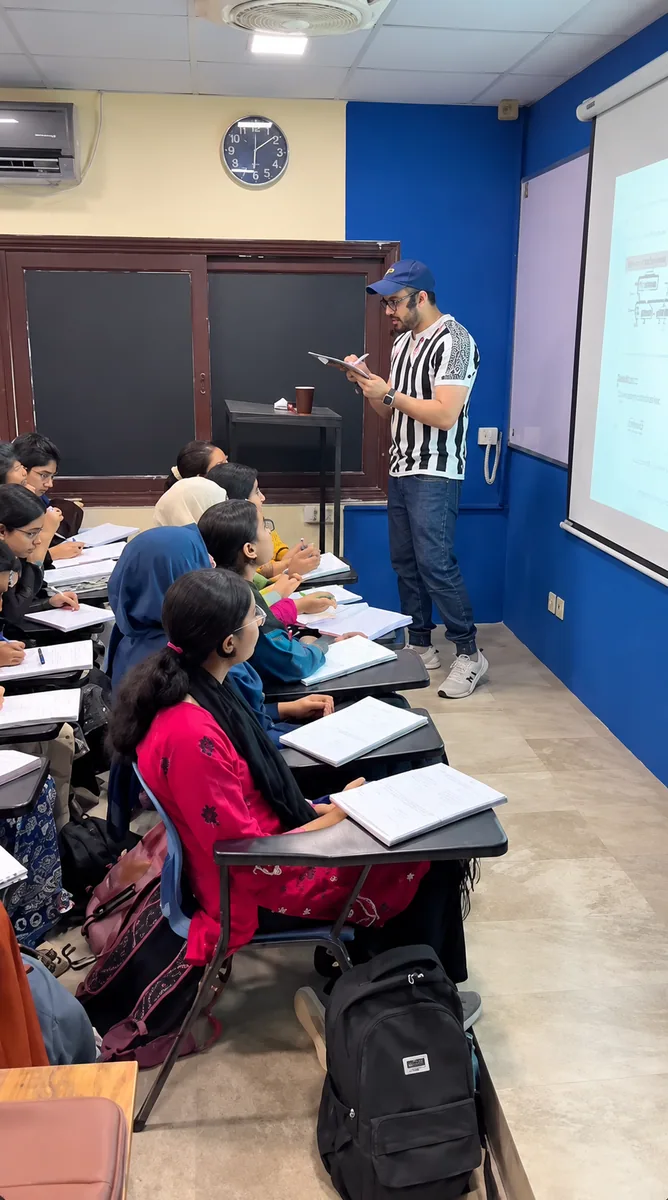 A teacher working through lesson notes beside students and a projection screen